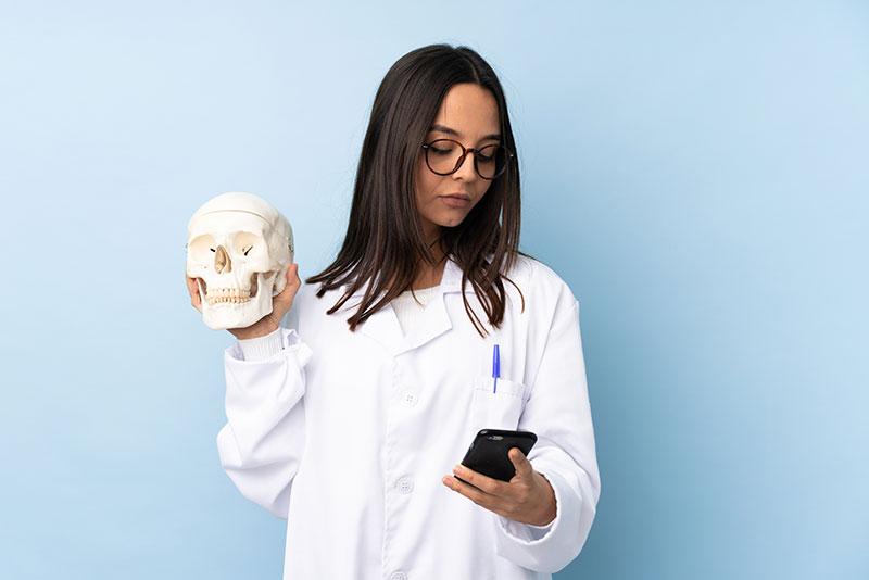aluna de medicina segurando um crânio na mão esquerda e um celular na mão direita
